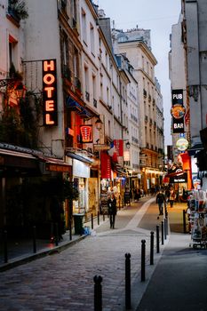 Bustling evening street scene in a European city with shops, restaurants, and pedestrians.