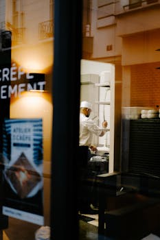 A chef working in a kitchen seen through a restaurant window, creating an intimate cooking scene.