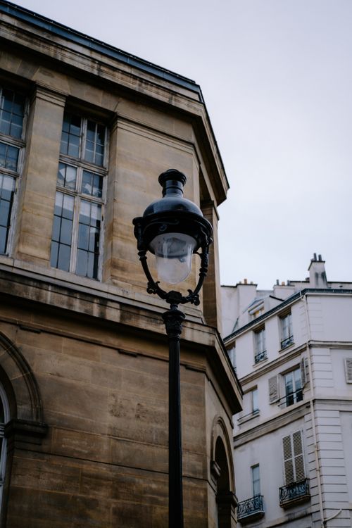 Free Classic Parisian street lamp beside historic architecture, capturing city charm. Stock Photo