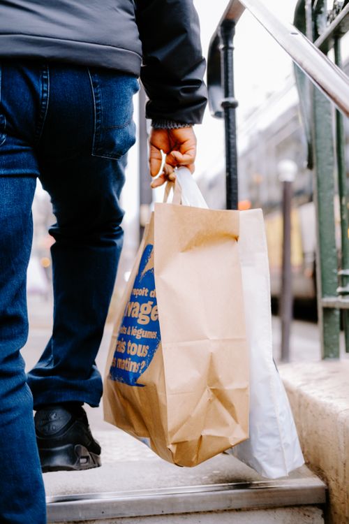 Free A man in blue jeans carrying paper and plastic bags while climbing stairs near metal railing. Stock Photo