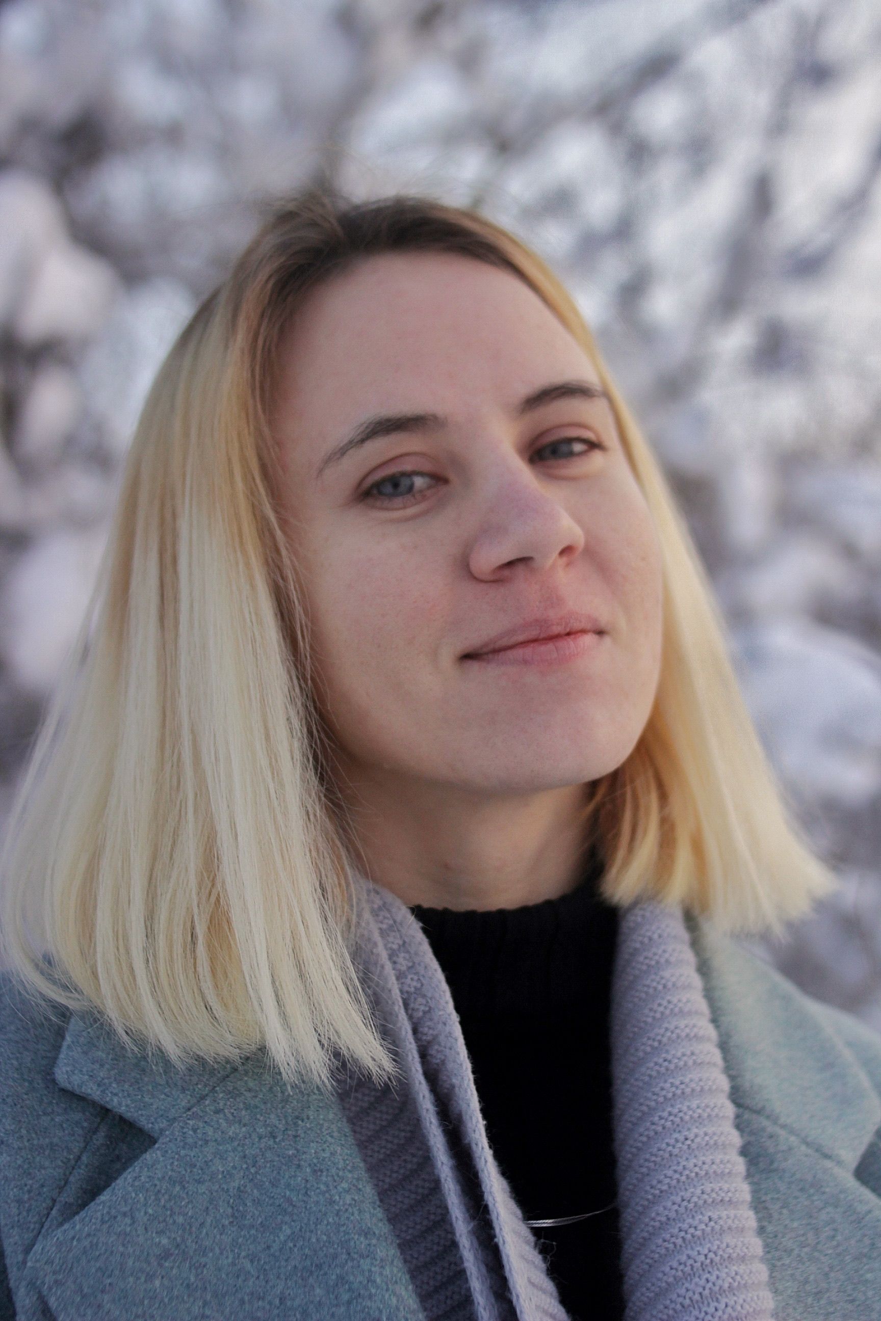 A cheerful woman in a winter setting wearing a gray coat and scarf, exuding warmth and confidence.