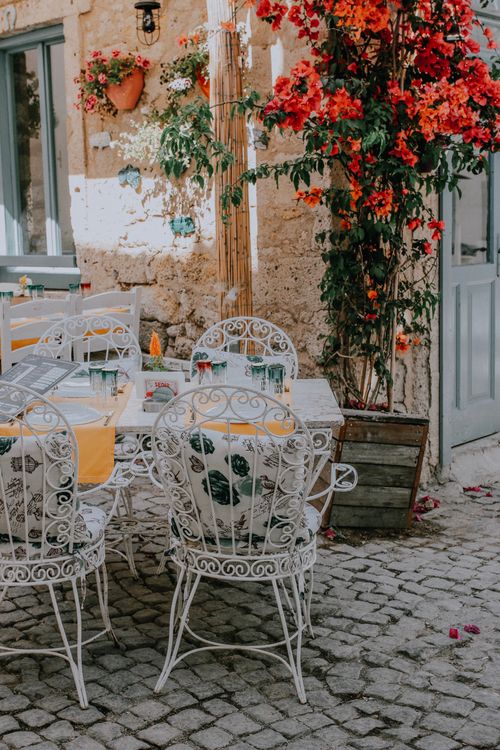 Free A quaint outdoor cafe setting featuring ornate chairs and vibrant bougainvillea. Stock Photo