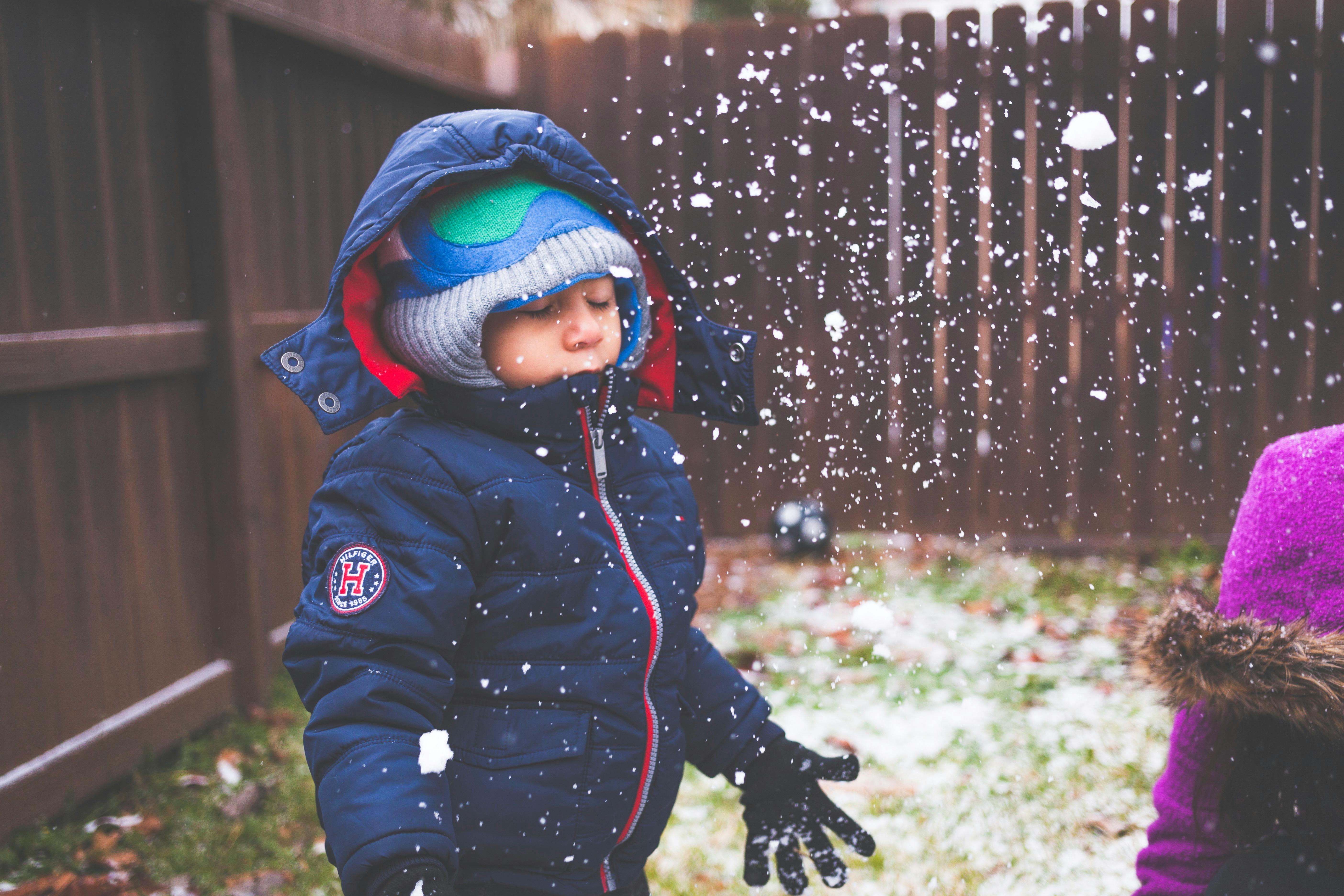 一个年幼的孩子穿着暖和的衣服，在后院享受白雪皑皑的冬日
