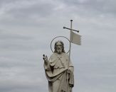 A serene marble statue of Jesus Christ with a cross against a backdrop of cloudy skies.