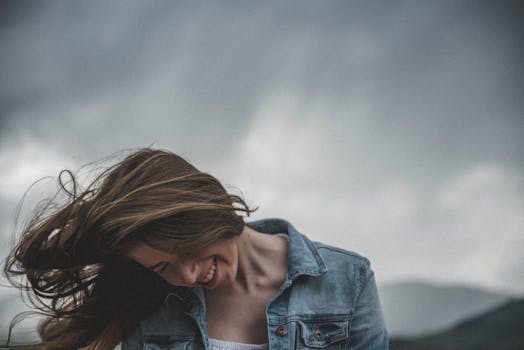 在基茨比尔，一位穿着牛仔夹克的年轻女子在刮风多云的天气里微笑着，拨弄着头发