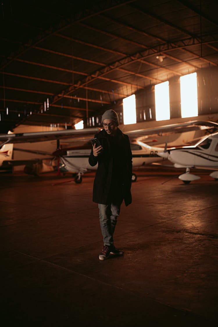 Man With Smartphone In Airplane Hangar