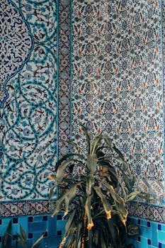 Stunning mosaic tile wall with intricate patterns and lush green plant in the foreground.