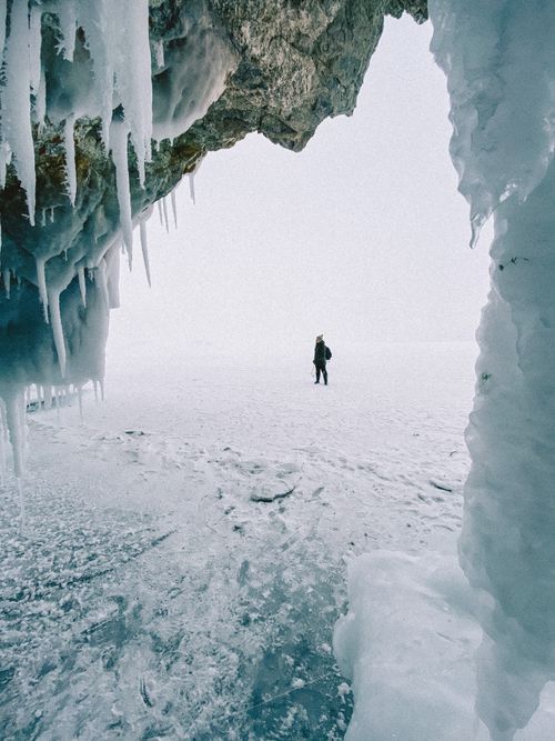 Free A solitary person walks across a snow-covered icy landscape framed by icicles. Stock Photo