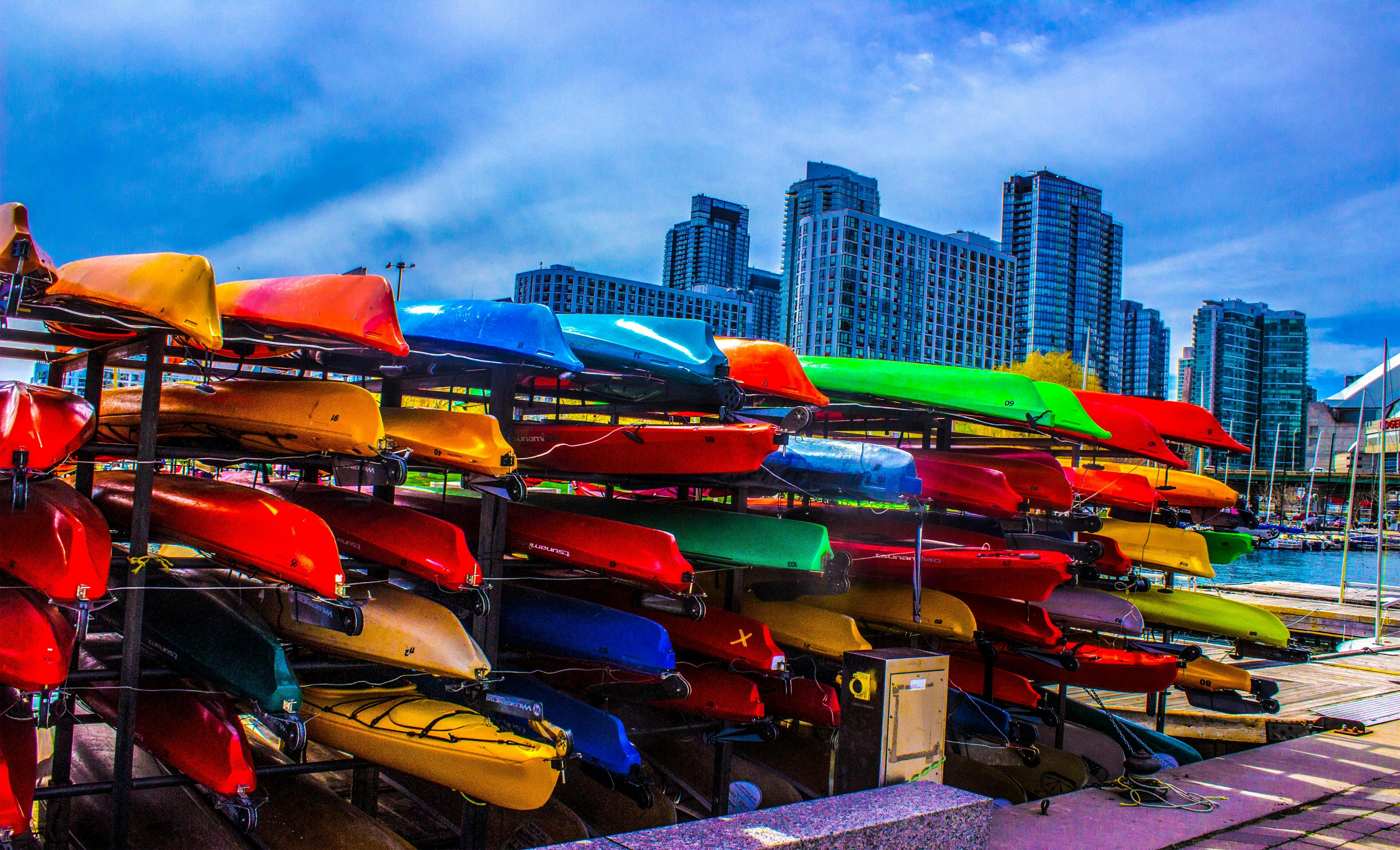 海滨上堆放着色彩缤纷的皮划艇，背景是城市天际线