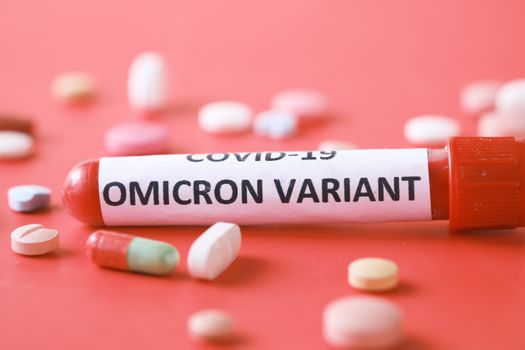 Close-up of Omicron variant test tube with assorted pills on a red background.