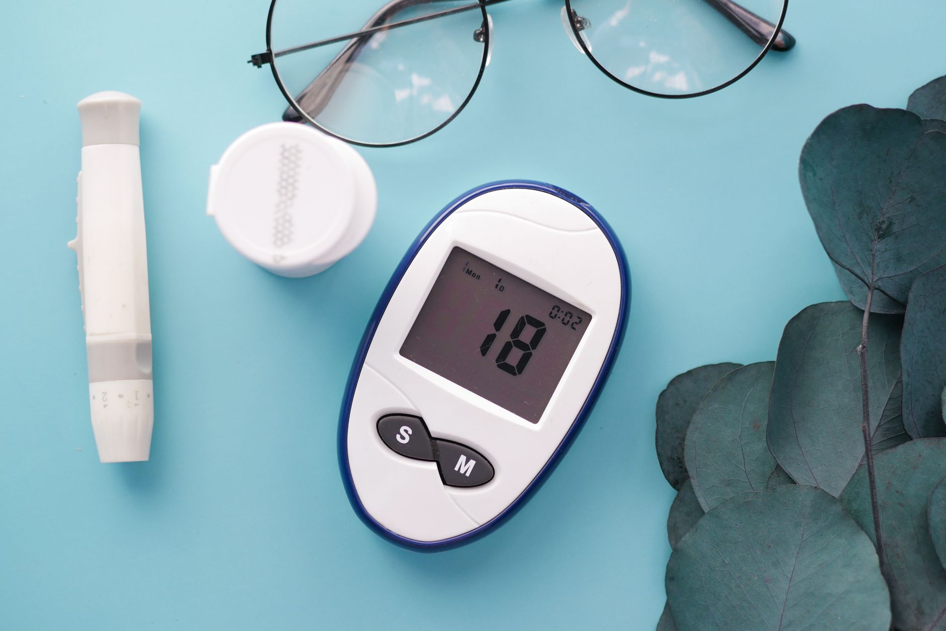 berberine for long covid blood sugar spikes — A top view of a glucometer, test strip, and glasses on a blue background, symbolizing health management.