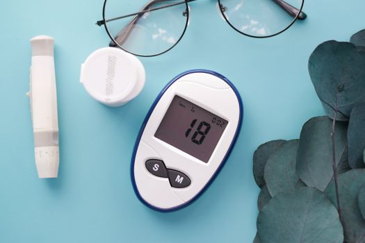 A top view of a glucometer, test strip, and glasses on a blue background, symbolizing health management.