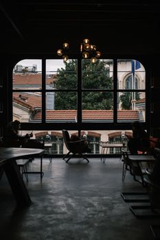 Cozy indoor café setting with patrons using phones, large windows showcasing a city view.