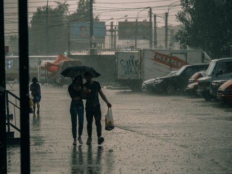 A couple walks under an umbrella during a heavy rain in an urban setting.