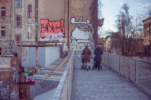 Free Mothers walking with strollers on graffiti-lined urban street bridge. Stock Photo