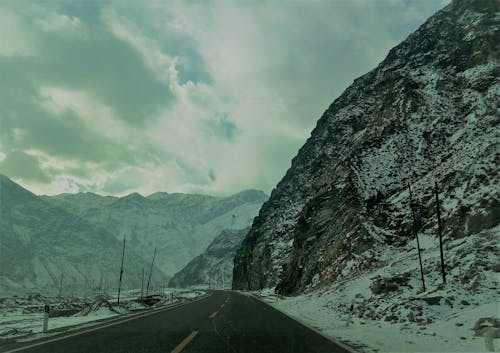 Snow Covered Mountain Ranges Near the Asphalt Road Under the Cloudy Sky