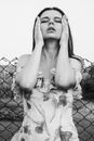 Woman in White and Black Floral Long Sleeve Shirt Leaning on Chain Link Fence