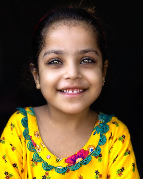 Free Adorable portrait of a young girl in a vibrant yellow dress with a joyful smile. Stock Photo