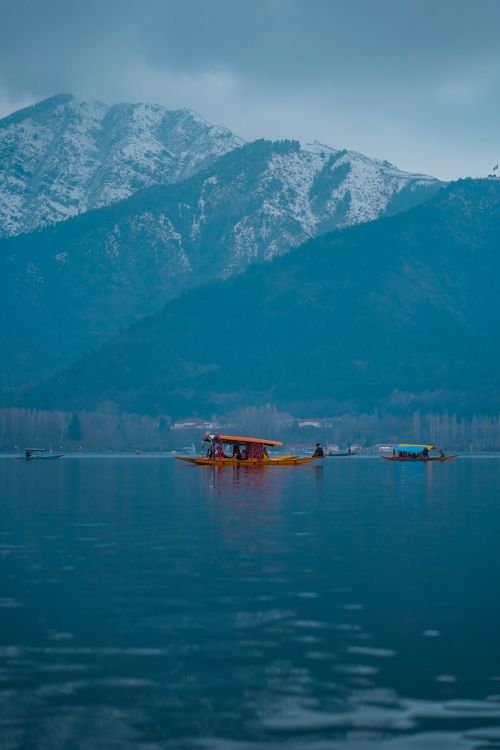 Free Tranquil scene of boats on a calm lake with majestic snow-covered mountains in the background. Stock Photo