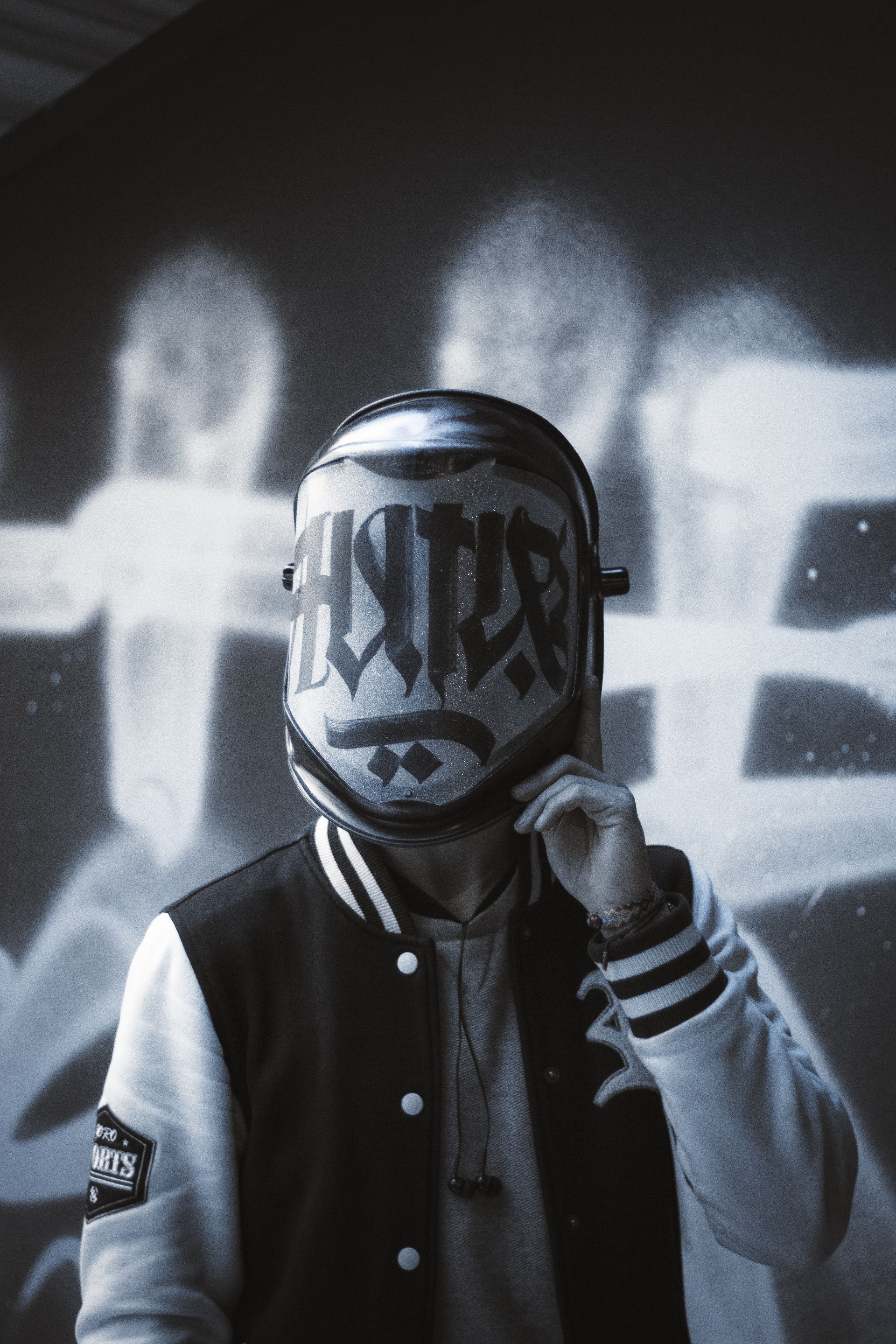 A person in an artistic mask stands before graffiti art, creating a mysterious atmosphere.