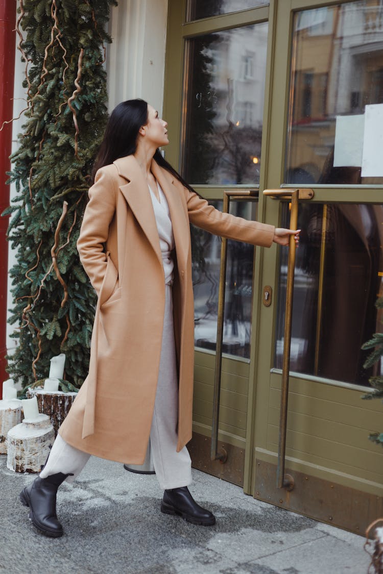 Woman In A Brown Coat Opening A Door