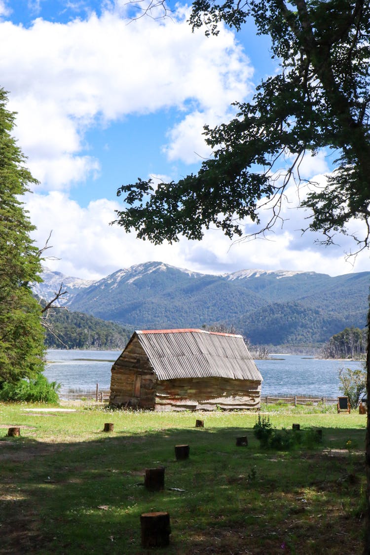 Wooden Cabin On River Bank In Mountains Landscape