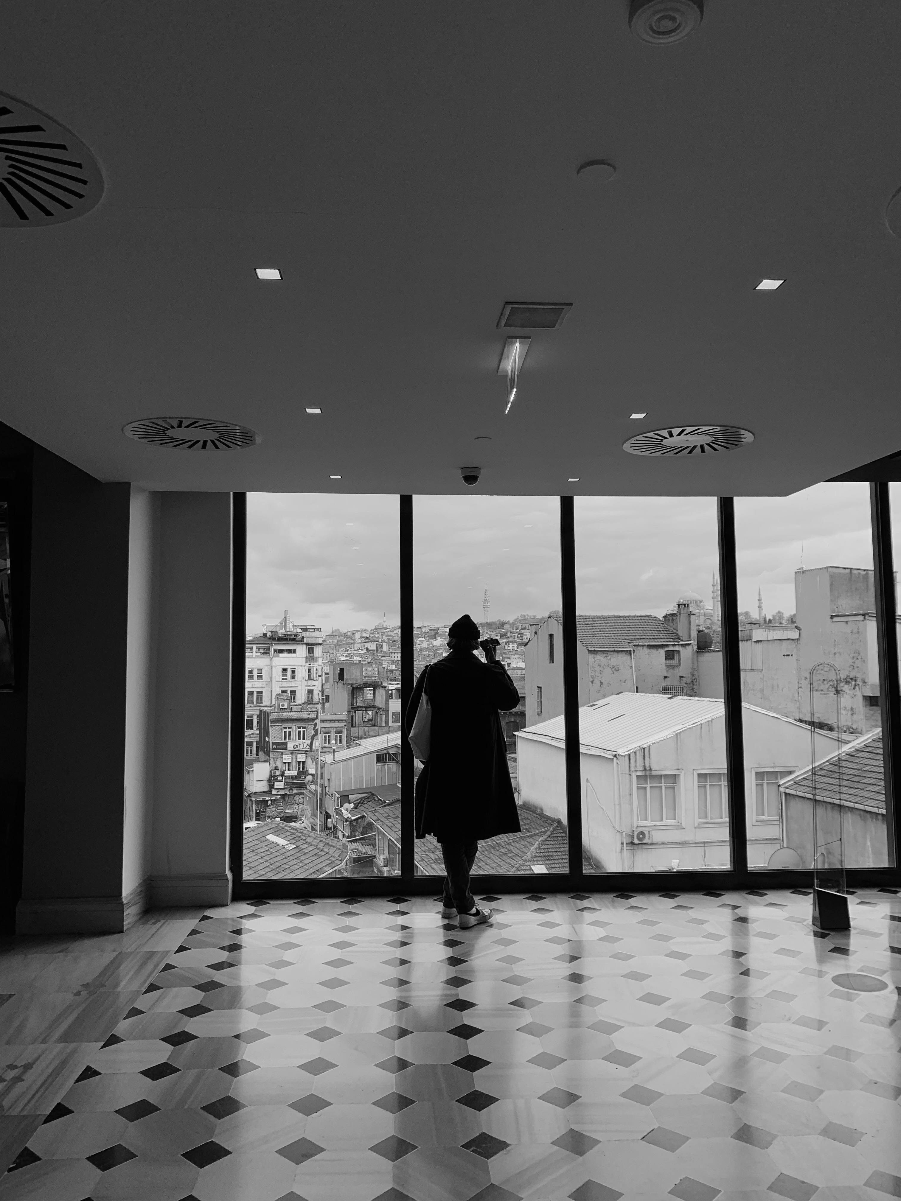 Grayscale photo of man standing near window photo – Free Cloud