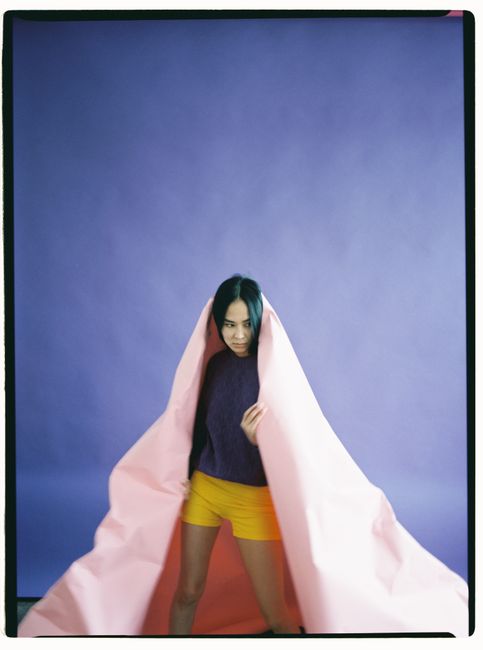 Woman posing with pink paper against a purple backdrop in a studio environment.