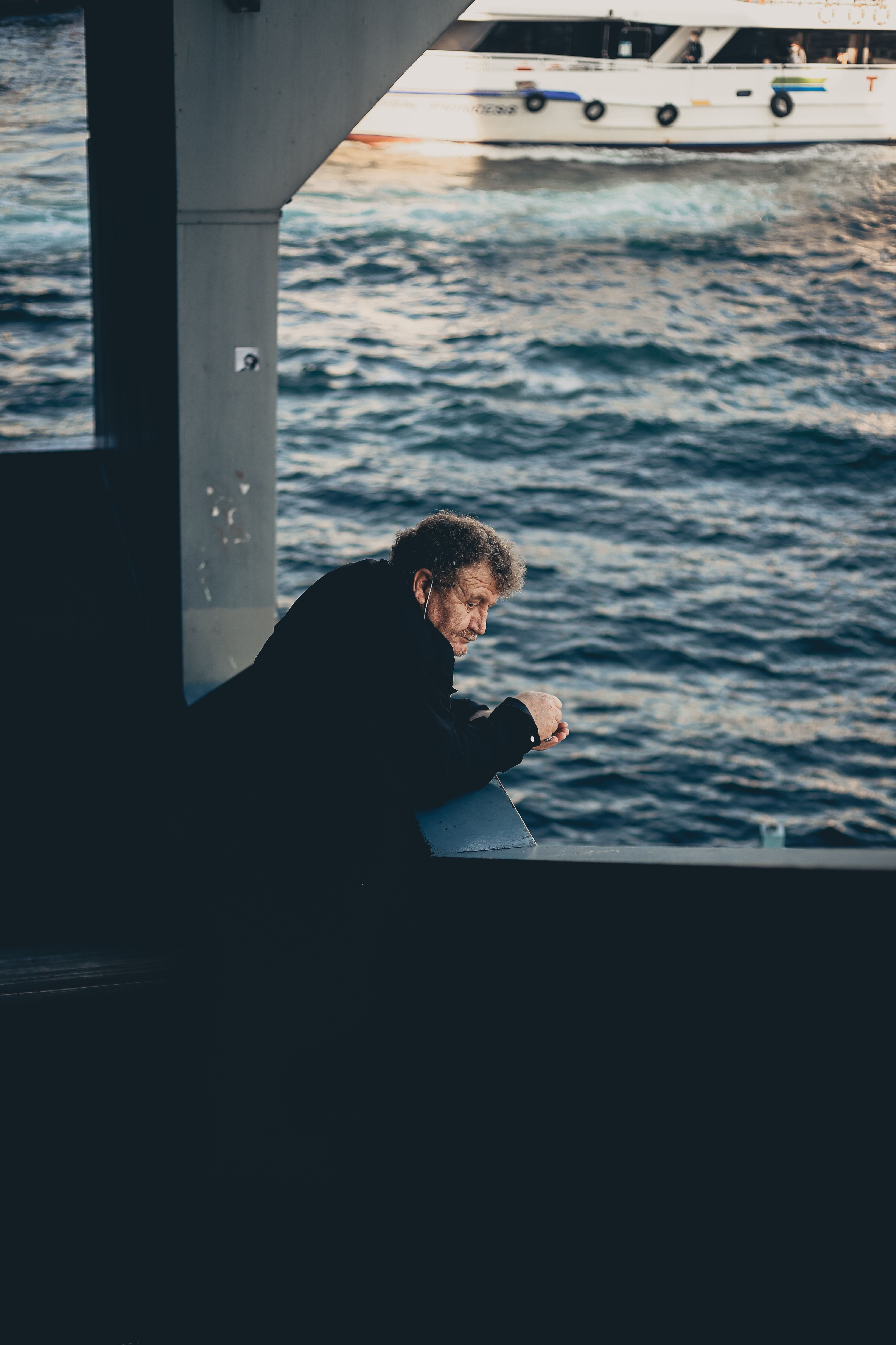 Senior man leans on Istanbul bridge railing, contemplating the Bosphorus view.