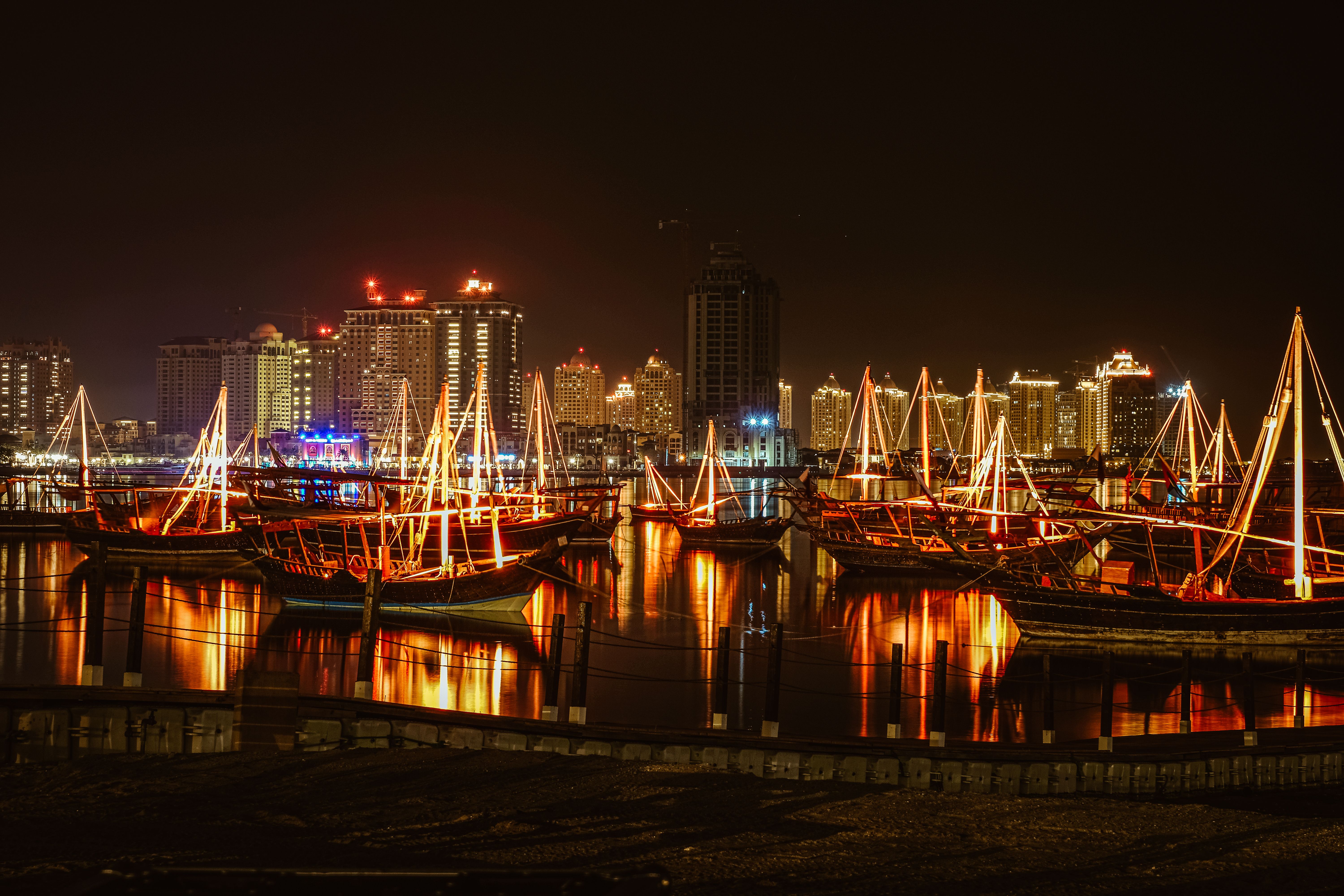 Stunning view of a city harbor at night, featuring illuminated sailboats and skyscrapers reflecting 