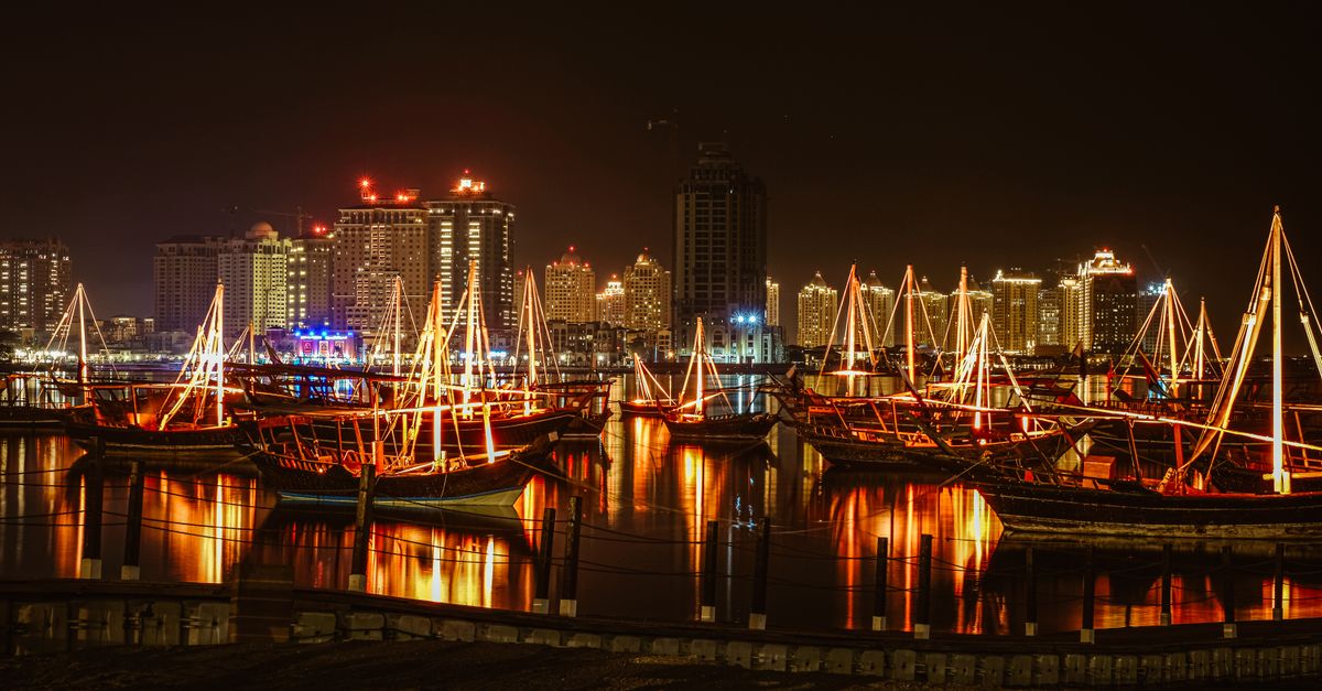 Stunning view of a city harbor at night, featuring illuminated sailboats and skyscrapers reflecting