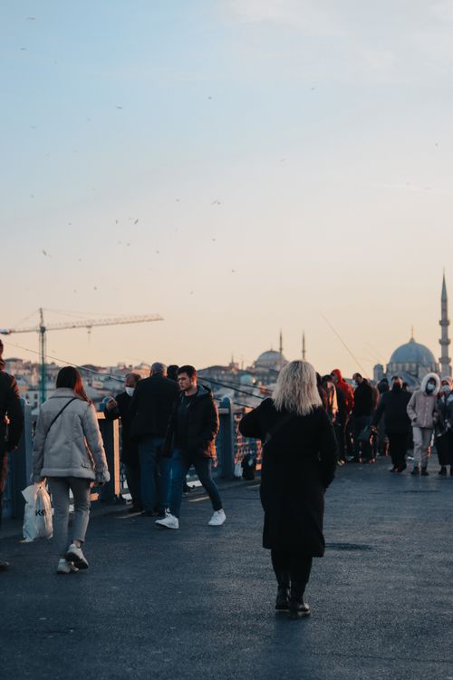 Free A diverse group of people strolls across a bridge at sunset with a city skyline in the background. Stock Photo