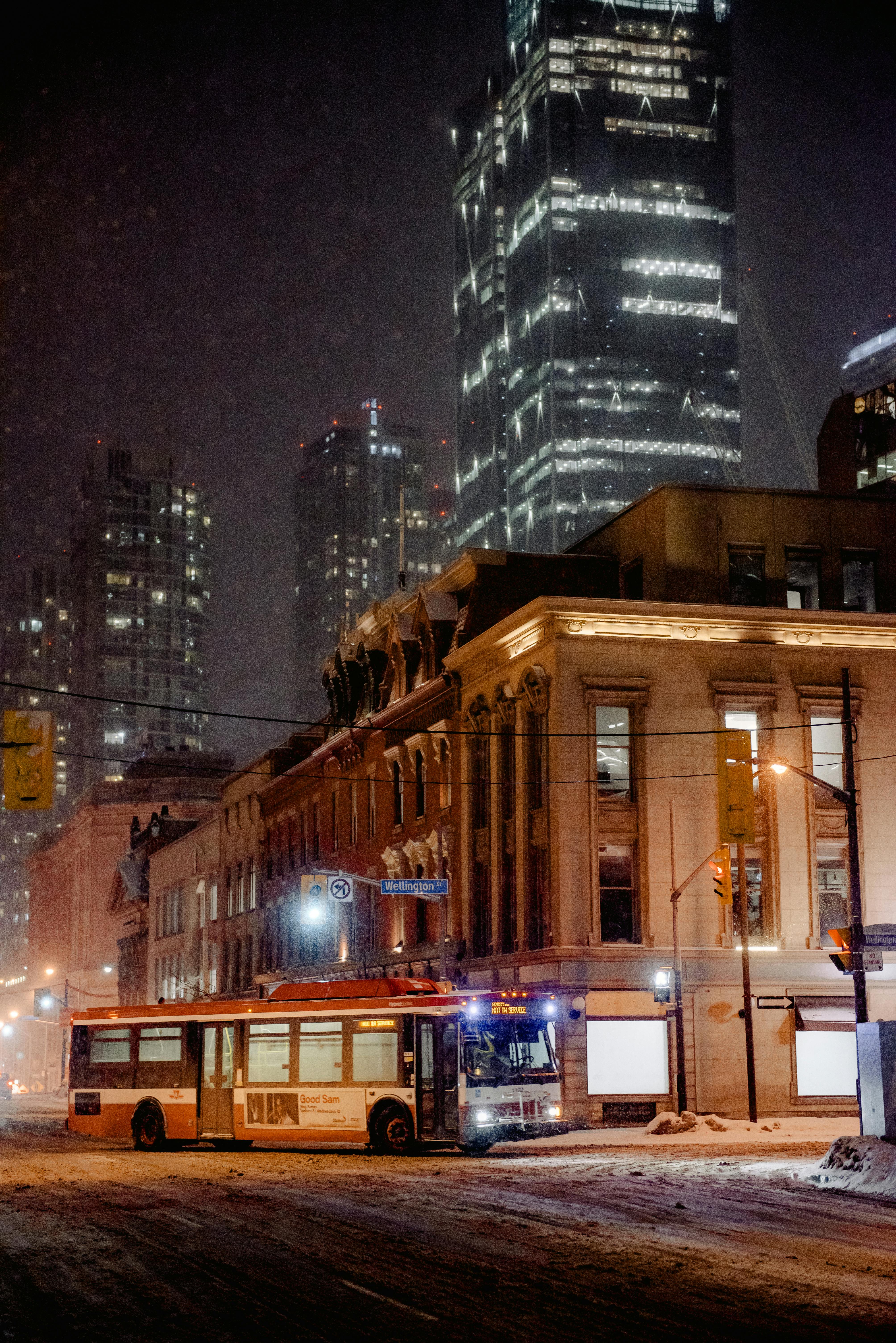 Free Snowy urban street with a bus passing by illuminated skyscrapers at night. Stock Photo