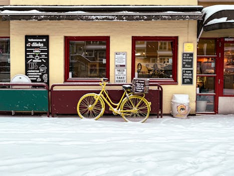 A vibrant yellow bike parked outside a Scandinavian cafe on a snowy winter street.