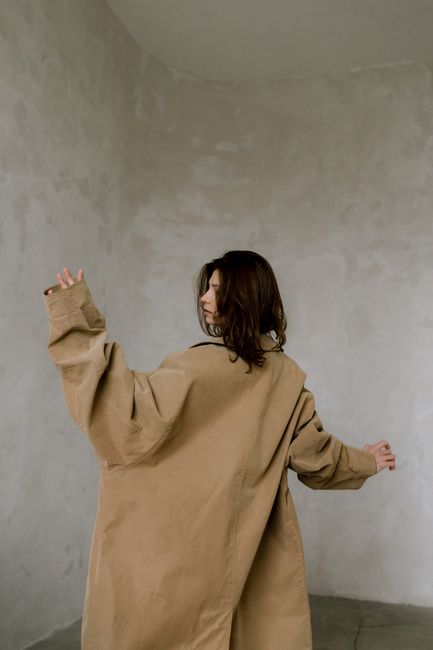 Elegant portrait of a woman in a large coat, posing with a creative touch indoors.