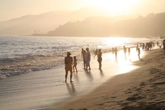 Captivating beach scene during sunset with silhouettes against shimmering ocean waves.