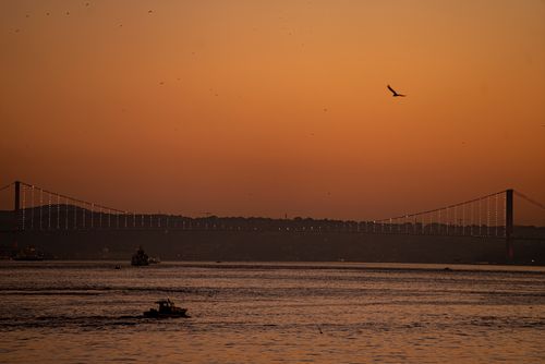 Free Scenic view of the Bosphorus Bridge at sunset with boats cruising in Türkiye's waters. Stock Photo