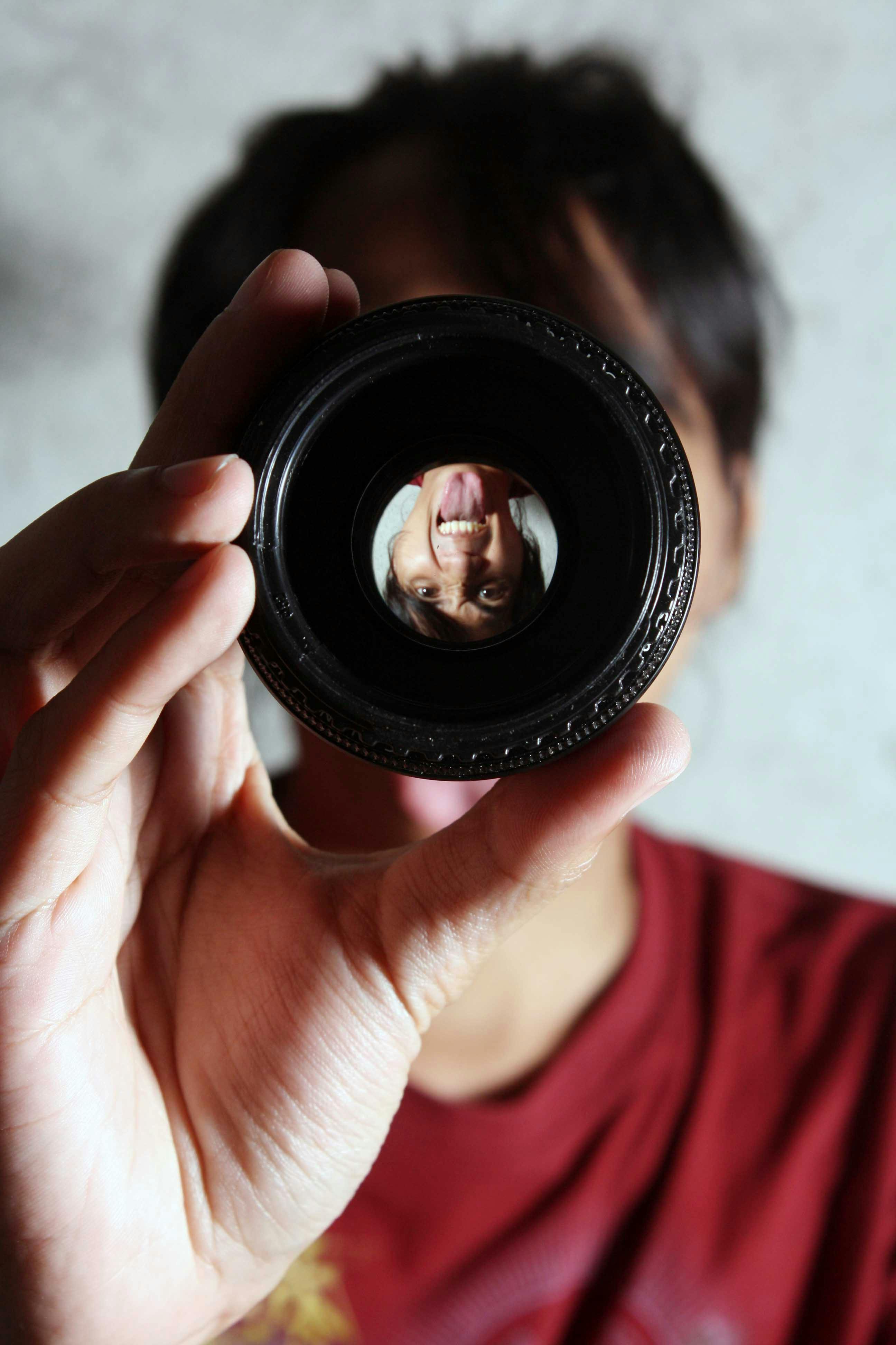 Artistic portrait of a person's reflection captured in a camera lens held by hand.