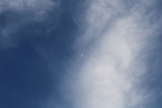 A serene daytime sky with white clouds framing a crescent moon.