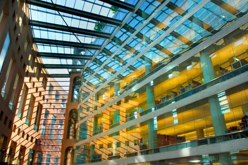 Free Vibrant interior of a modern office building with glass ceilings and sunlight filtering through. Stock Photo