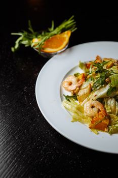 Close-up of a fresh shrimp salad with lettuce and orange slices on a white plate.