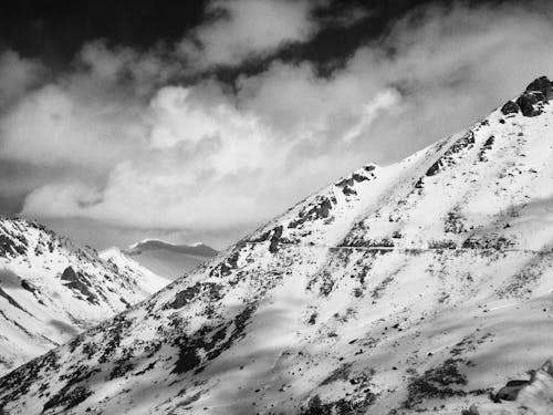 Grayscale Photo of Snow-Covered Mountains under the Cloudy Sky