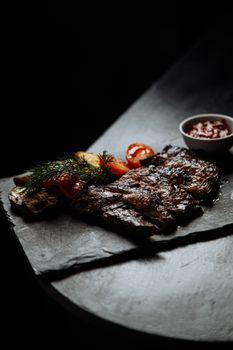 Succulent grilled steak with roasted veggies and sauce on a slate plate.