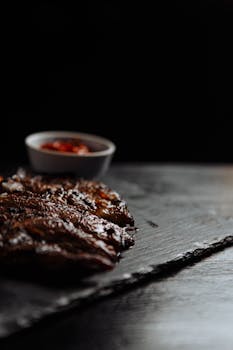 Indulgent grilled steak with a side of sauce, captured in a low-light, moody setting.
