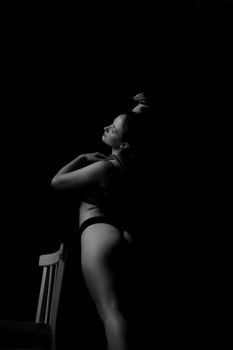 Artistic black and white photo of a nude woman posing dramatically in shadows.