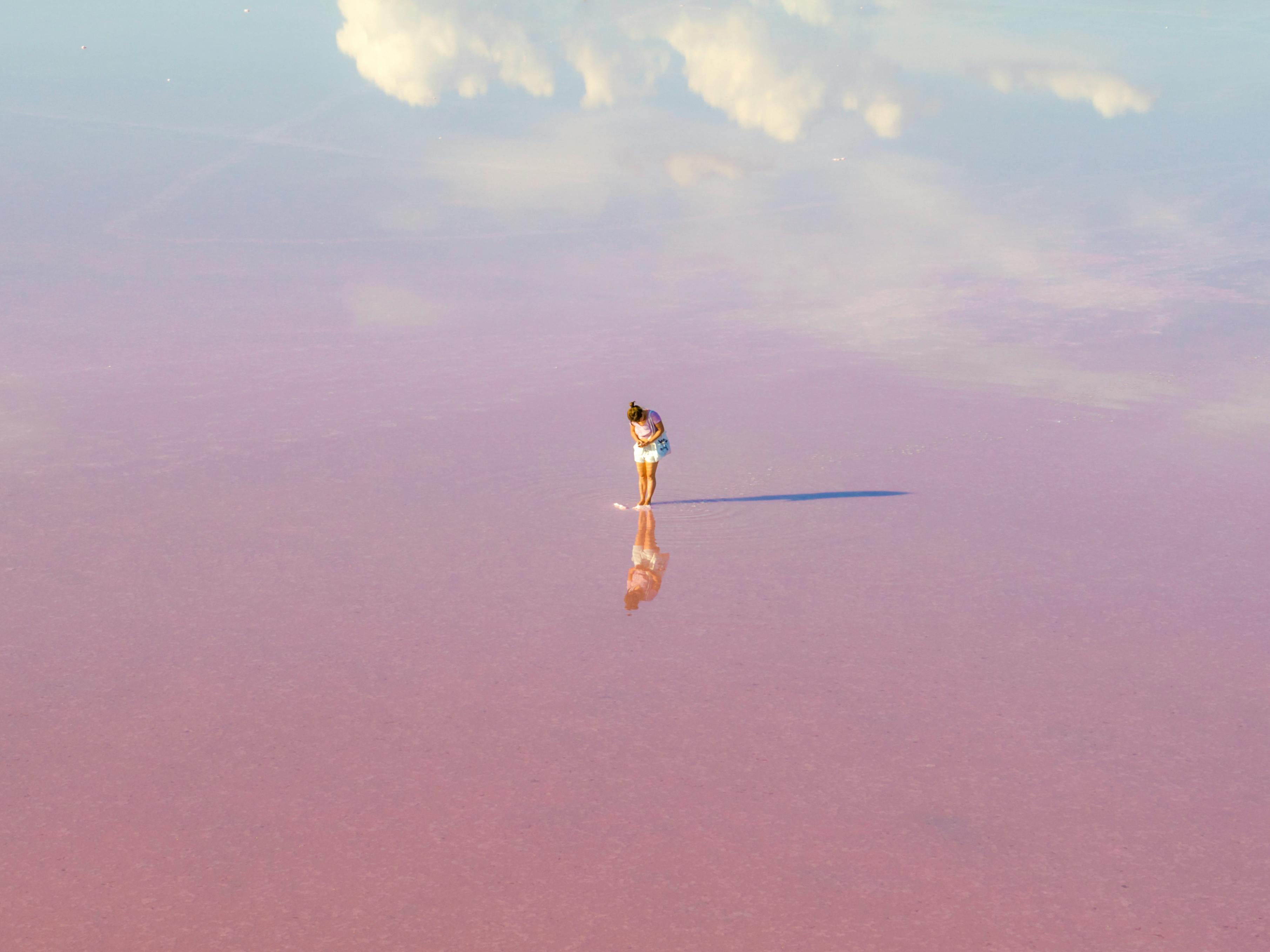 A woman stands on a vast pink salt lake, reflecting clouds in Dimboola, Australia.