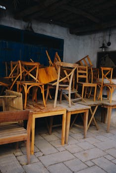 A collection of wooden chairs stacked outside against a rustic blue door.
