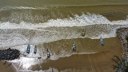 Free Drone shot capturing boats on a sandy shoreline with gentle waves. Stock Photo