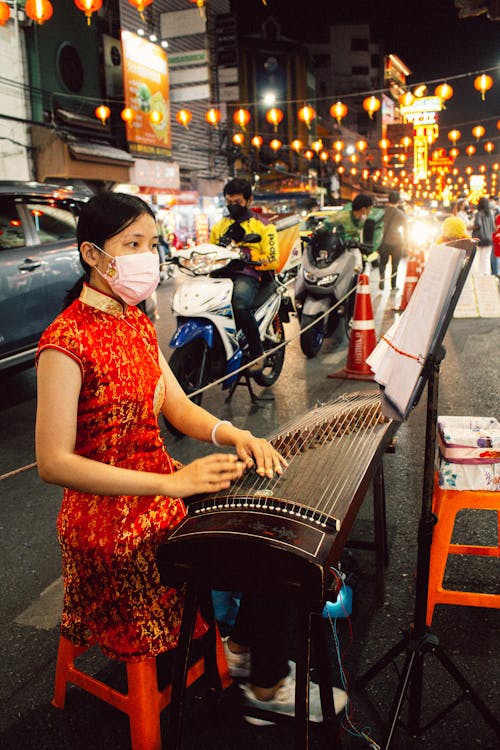 A Woman in Red Traditional Clothing Playing Stringed Instrument on the Street