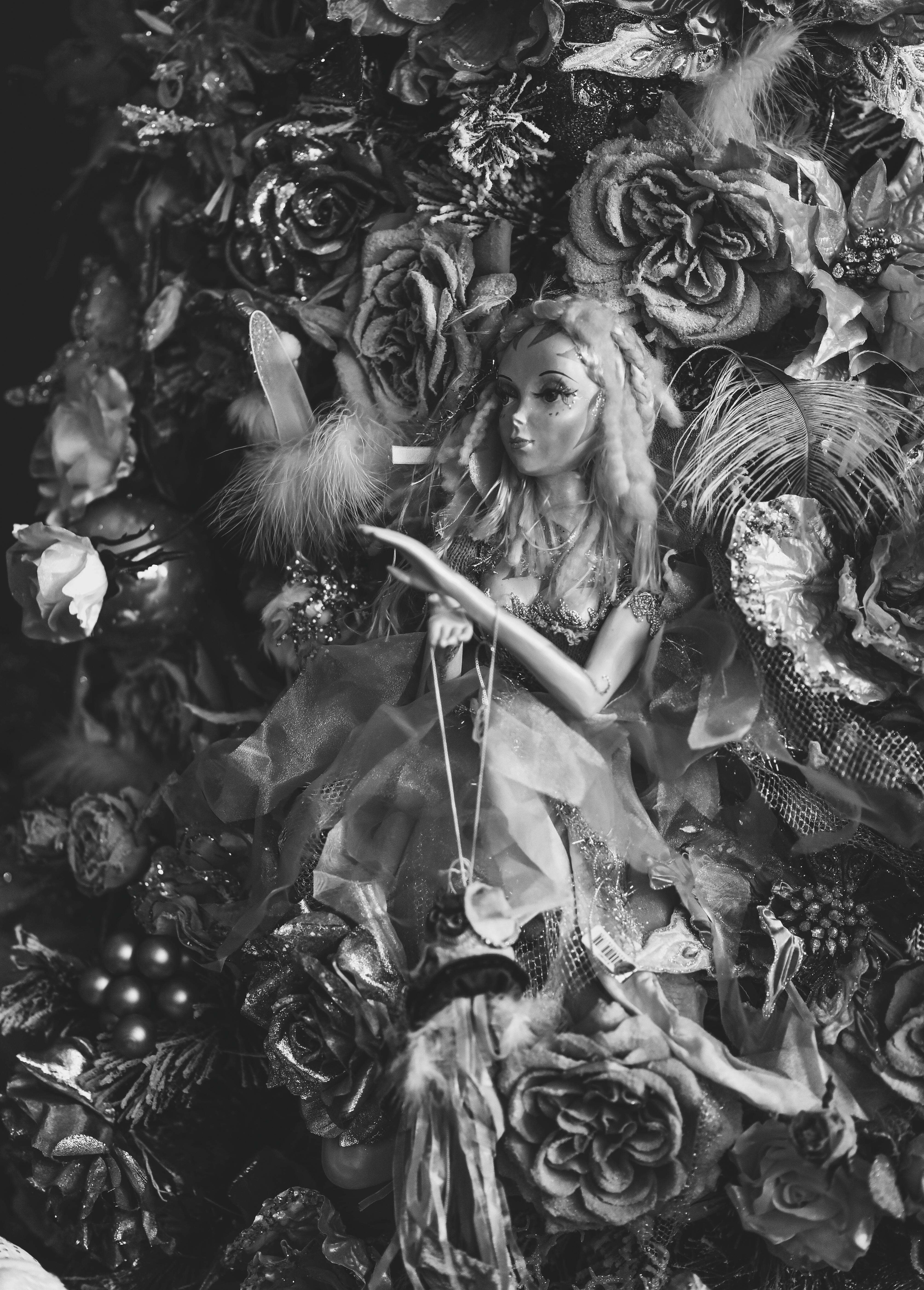 grayscale photography of a doll surrounded with flowers